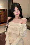 Woman wearing an off-shoulder beige top with decorative elements in a room.