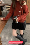 Person wearing a red sweater with bow details and a black skirt, holding a coffee cup in a casual setting.