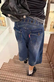 A person wearing blue denim shorts with a distinctive curved pocket design and a striped shirt, standing on an indoor tiled staircase.