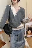 Person wearing a gray and white sweater with blue jeans, holding a black bag indoors.