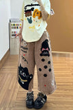 Person wearing a white t-shirt with colorful graphics and brown pants with black cat designs indoors.