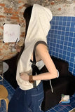 Person wearing a white hoodie and blue overalls sitting in a casual setting with a brick wall and blue tiles.