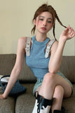 Woman sitting on a couch wearing a blue sleeveless top and denim shorts with suspenders.