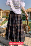 Person wearing a white t-shirt with text and a plaid skirt, standing by a poolside.