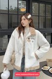 Woman wearing a white and beige jacket with patches, standing outdoors.