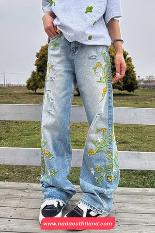 Person wearing light blue jeans with floral embroidery in an outdoor setting.