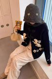 Person wearing a dark sweater with bunny designs, light pants, and a gray hooded hat, sitting on a floor.