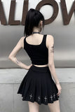 Person wearing a black sleeveless top and pleated skirt with cross designs, standing against a neutral wall.