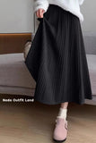 Person wearing a black pleated skirt and white sweater, standing in a room with a couch.