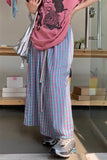 Person wearing a pink shirt and plaid pants in a room with shelves and boxes.