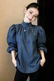 Woman wearing a blue denim blouse with puffed sleeves against a neutral background