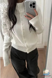 Person wearing a white cardigan and black pants, holding a phone.