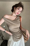Woman wearing a beige top and white skirt with a brown handbag indoors.