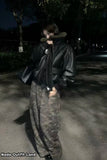 Person wearing a black coat and camouflage pants standing on a street at night.