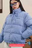 Person wearing a blue checkered puffer jacket with a visible brand logo, standing against a neutral background.