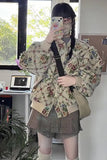 Person wearing a floral shirt and plaid skirt taking a mirror selfie in an indoor setting.
