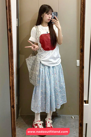 Woman taking a mirror selfie wearing a white t-shirt with a red pocket design, light blue floral skirt, and red sneakers.