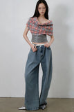 Person wearing a plaid top and blue jeans against a plain background