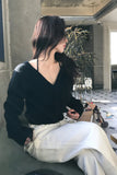 Woman sitting on a couch wearing a black sweater and white pants in an indoor setting.