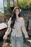 Woman wearing a floral off-shoulder blouse and light gray pants outdoors.