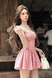 Woman in a pink checkered dress holding a white handbag in an indoor setting.