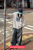 Person wearing a white t-shirt with text and graphics, standing on a street corner.