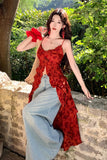 Woman in a red dress and light blue jeans sitting on a stone wall with greenery in the background