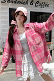 Woman wearing a pink plaid jacket and cap in front of a 'Sandwich & Coffee' shop.