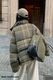 Person wearing a plaid jacket and holding a green bag, standing on a street.