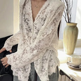 Person wearing a white lace kimono-style garment in a room with a vase and cup on a table.