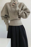 Person wearing a beige sweater and black skirt against a white background