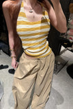 Person wearing a yellow and white striped tank top and beige pants indoors.