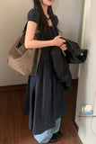 Woman in a plaid dress holding a beige bag and black jacket indoors.