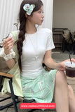 Woman in a white top and green skirt holding a drink, with a blurred background