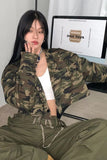 Person wearing a camouflage jacket and green pants sitting in front of a computer screen.