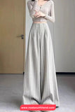 Woman wearing a light-colored outfit with a long skirt in a minimal setting.