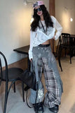 Person wearing a white oversized shirt, gray plaid pants, and black shoes in a casual setting.
