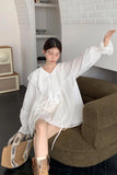 Woman in a white outfit sitting on a brown chair in a room with a white brick wall.