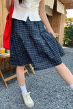 Person wearing a blue plaid skirt and white shirt outdoors.