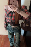 Person wearing a plaid jacket and jeans, holding a phone with a visible brand logo.