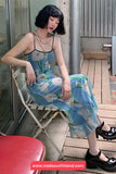 Woman in a floral dress sitting on a chair outdoors, with a visible brand name at the bottom.
