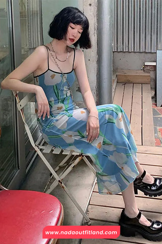 Woman in a floral dress sitting on a chair outdoors, with a visible brand name at the bottom.