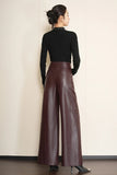 A woman shown from the back wearing a black long-sleeve mock neck top and high-waisted, wide-leg brown faux-leather pants, standing against a light beige wall.