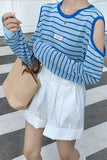 Person wearing a blue and white striped long-sleeve top with cut-out shoulders, holding a beige handbag on a striped floor.