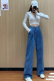 Person wearing a white long-sleeve top and blue high-waisted jeans taking a mirror selfie against a wooden wall.