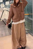 Person wearing a brown knitted cardigan and plaid pants in an indoor setting.