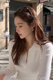 Woman with long brown hair wearing a white blouse sitting outdoors.