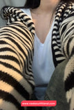 Person wearing a zebra-striped cardigan over a white shirt with a visible brand logo.