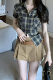 Woman wearing a plaid shirt and beige skirt in an indoor setting