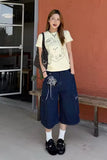 Woman wearing a white t-shirt with graphics and blue patterned pants standing against a red wall.